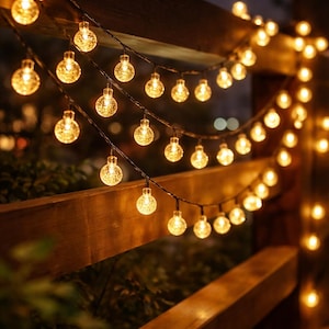 Puede incluir: Cadena de luces globulares cálidas y brillantes colgadas sobre una valla de madera. Las luces redondas, con superficie texturizada, emiten un brillo suave y acogedor sobre un fondo oscuro. Perfectas para la decoración exterior.