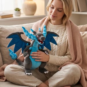 May include: A plush Charizard toy in shades of gray, blue, and red. The dragon-like creature has large blue wings, a blue belly, and a flame-shaped tail. The toy is soft and cuddly, perfect for fans of the popular franchise.