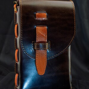 May include: A dark brown leather pouch with a smooth finish, featuring a lighter tan leather strap closure and side lacing. The bag has a flap top, visible stitching, and metal hardware at the top corners. Text reads Full Tutorial & PDF Download.