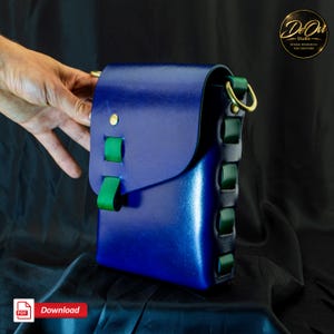 May include: A structured blue leather bag featuring a flap closure secured with a gold-toned metal stud. The bag is accented with vibrant green leather loops along the side and front flap, and includes gold-toned metal D-rings for strap attachment.