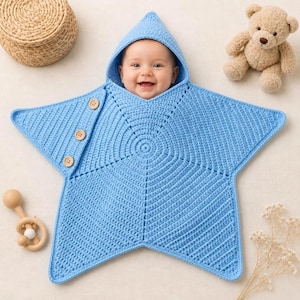 May include: A light blue star-shaped crochet baby blanket with a hood. The blanket features a textured stitch pattern and three wooden buttons along one side. The design is shaped like a five-pointed star, providing a cosy wrap for an infant.