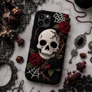 Può includere: Custodia per telefono nera con un teschio all'uncinetto, rose rosse e un disegno a ragnatela. La custodia è decorata con foglie e viti nere e verdi. Lo sfondo include rose secche, pizzo e uncinetti.