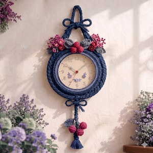 May include: A round wall clock framed in dark blue braided rope with a cream-colored face featuring black numerals. The clock is decorated with crocheted pink flowers, grey leaves, and red berries, with a matching rope tassel hanging below.