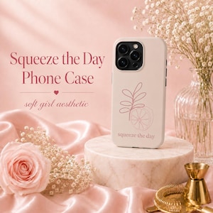 Könnte beinhalten: Eine hellrosa Handyhülle mit einer dunkelrosa Strichzeichnung einer Zitronenscheibe mit Blättern und dem Text "squeeze the day" am unteren Rand. Die Hülle verfügt über einen Kameraausschnitt und steht auf einem runden Marmorsockel.