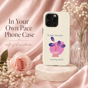 Könnte beinhalten: Eine cremefarbene Handyhülle mit einer Grafik einer Topfpflanze mit dunkelblauen Blättern und einem rosa Topf. Der Text "In your own pace" steht über der Pflanze und "everything unfolds" steht darunter in dunkelblauer Schrift.
