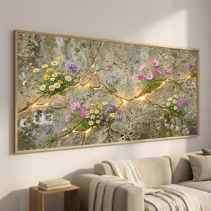 May include: A framed wall art piece featuring a cracked stone design with glowing gold-colored fissures. Colorful flowers, including daisies and cosmos, bloom from the cracks. The artwork is in a wooden frame and hangs above a beige sofa.