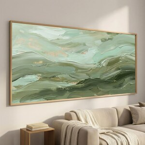 May include: Abstract landscape painting with a palette of greens and beige tones. The artwork features textured brushstrokes, creating a sense of depth and movement. The painting is framed in a light wood frame, adding a natural touch to the decor.