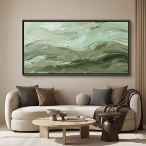 May include: Abstract oil painting in shades of green and gold, framed in black. The artwork features textured brushstrokes creating a sense of movement and depth. The painting is displayed above a cream-colored sofa with decorative pillows.