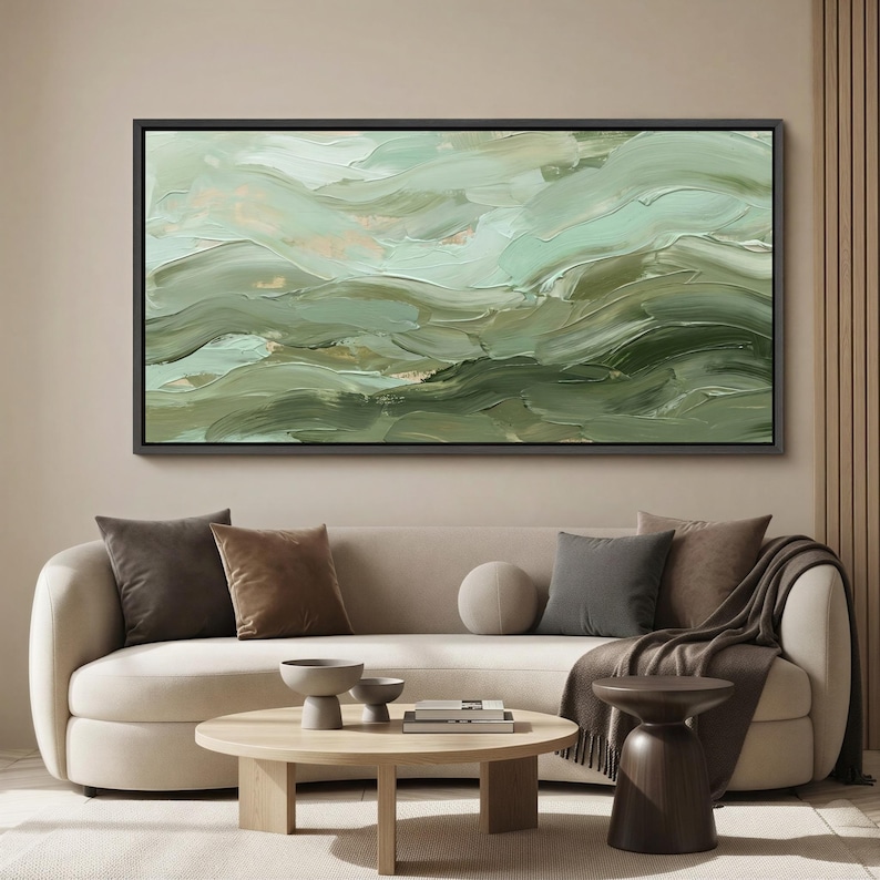 May include: Abstract oil painting in shades of green and gold, framed in black. The artwork features textured brushstrokes creating a sense of movement and depth. The painting is displayed above a cream-colored sofa with decorative pillows.