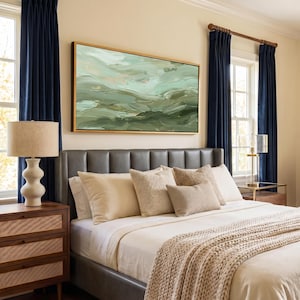 May include: A bedroom scene featuring a bed with a gray leather headboard, cream-colored bedding, and decorative pillows. A large abstract painting in shades of green and gold hangs above the bed. Navy blue curtains frame the windows.