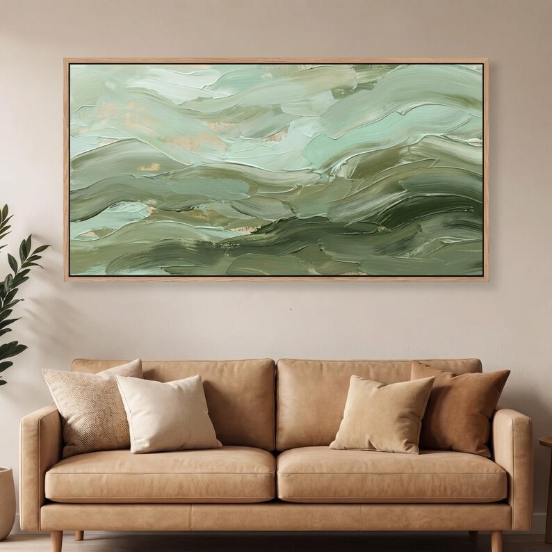 May include: Abstract landscape painting in shades of green and gold. The artwork features textured brushstrokes creating a sense of movement and depth. The painting is framed in a light-colored wooden frame, adding a touch of warmth to the piece.