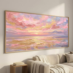 May include: A rectangular landscape painting in a thin gold frame featuring an abstract sunset over water. The artwork uses thick, textured impasto brushstrokes in shades of soft pink, golden yellow, lavender, and muted blue across the sky and sea.