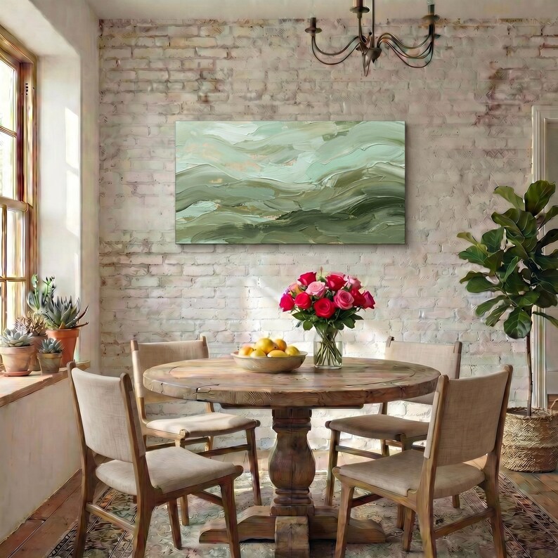 May include: A dining room scene featuring a round wooden table with four chairs. A vase of red and pink roses sits on the table. A landscape painting in shades of green hangs on the brick wall.