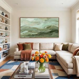 May include: A living room with a large beige sectional sofa, a coffee table, and a colorful rug. A large abstract painting in shades of green and gold hangs above the sofa. A vase of orange and yellow flowers sits on the coffee table.