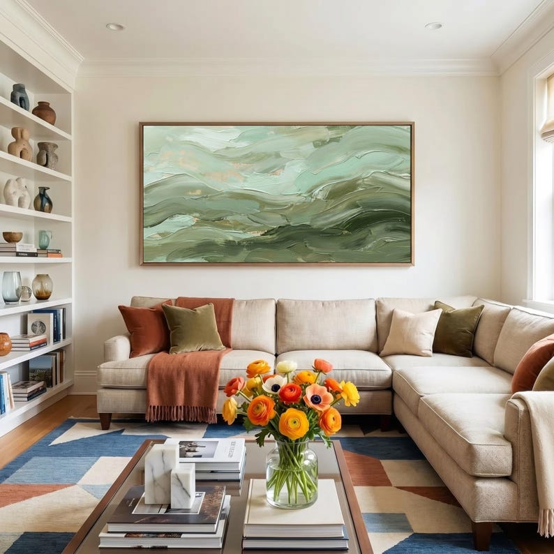 May include: A living room with a large beige sectional sofa, a coffee table, and a colorful rug. A large abstract painting in shades of green and gold hangs above the sofa. A vase of orange and yellow flowers sits on the coffee table.