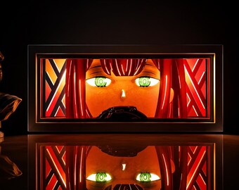 Könnte beinhalten: Ein rechteckiger Leuchtkasten mit einer hinterleuchteten Grafik einer Figur mit leuchtend rotem Haar und markanten grünen Augen. Das Design umfasst geometrische rote und orangefarbene Muster im Hintergrund, eingefasst in einen schwarzen Rahmen.