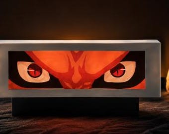Könnte beinhalten: Ein rechteckiges, beleuchtetes Kunstwerk mit einem stilisierten Bild von feurigen orangefarbenen Augen mit roten Iris. Das Kunstwerk ist in einem silbernen Rahmen eingefasst und ruht auf einem schwarzen Sockel, wodurch ein auffälliger Kontrast vor einem warmen, dunklen Hintergrund entsteht.