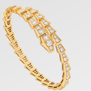 Puede incluir: Un brazalete dorado con diseño de serpiente, con segmentos triangulares. Cada segmento está adornado con múltiples gemas claras y brillantes. El brazalete se enrolla sobre sí mismo, creando un aspecto lujoso y elegante.