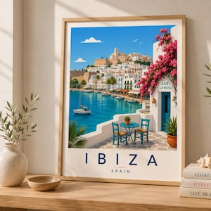 Puede incluir: Una impresión artística enmarcada de Ibiza, España, que presenta una escena costera con edificios blancos, un mar azul y un velero. La impresión incluye la palabra "IBIZA" en azul marino y el texto "SPAIN" debajo. Un café es visible con el texto "CAFE LA VISTA".