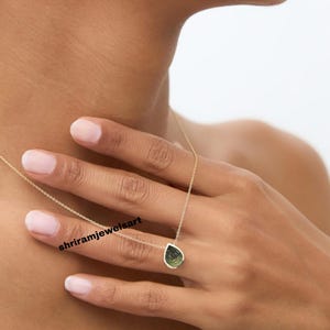 May include: A gold necklace with a teardrop-shaped pendant. The pendant features a green and black stone. The necklace is delicate and appears to be worn around the neck.