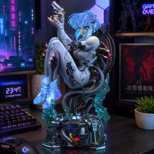May include: A detailed figurine of a character with blue hair, wearing a white suit, and holding a gun. The figure is seated on a complex mechanical base with glowing blue accents. The background includes a computer monitor with Japanese text and a digital clock.