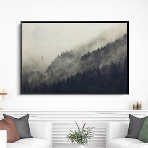 May include: A framed landscape art print depicting a misty forest scene. The artwork features a dark, dense forest with fog rolling through the trees. The print is displayed above two white sofas in a modern living room setting.