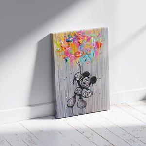 Peut inclure: Impression sur toile repr&eacute;sentant Mickey Mouse tenant des &eacute;claboussures de peinture color&eacute;es. L'&oelig;uvre d'art est en noir, blanc et gris avec des &eacute;claboussures vibrantes de rose, jaune, bleu et vert. Le mot "EX" est visible dans la peinture.