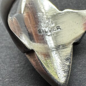 Op de afbeelding: Close-up van een zilverkleurig metalen object met het woord "SILVER" erop gestempeld. Het object heeft een stervorm met puntige randen en een getextureerd oppervlak. Het metaal lijkt gepolijst en reflecterend.