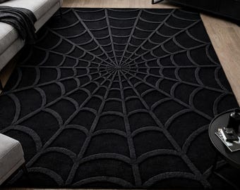 May include: A rectangular area rug featuring a solid black color and a raised, textured spider web pattern that radiates from the center toward the edges. The design consists of concentric circular lines connected by straight radial lines.