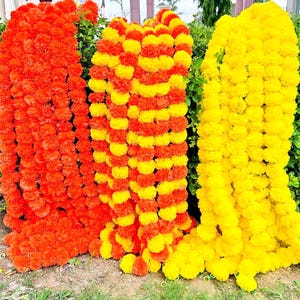 Puede incluir: Tres guirnaldas de caléndulas en colores vibrantes. Una es naranja sólido, otra alterna amarillo y naranja, y la tercera es amarillo sólido. Las guirnaldas están densamente llenas de flores, creando una apariencia completa y texturizada.
