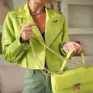Può includere: Giacca e borsa abbinate in ecopelle verde lime. La giacca, in stile biker, ha una chiusura con zip e dettagli dorati. La borsa, di forma rettangolare, ha una tracolla a catena dorata e una chiusura a fermaglio.