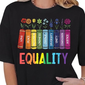 May include: Black t-shirt with a colorful graphic. The design features a row of books with words like "Love" and "Equality" printed on them, topped with flowers. The word "EQUALITY" is printed in rainbow colors.