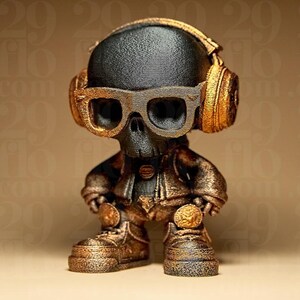 May include: A small, stylized figurine of a skull wearing headphones and glasses. The figure is primarily black and gold, with the headphones, glasses, jacket, and boots in a metallic gold finish. The skull has its hands on its hips.