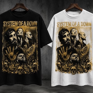 以下が含まれることがあります： 黒いTシャツと白いTシャツ。それぞれにバンド「System of a Down」のゴールドトーンのグラフィックプリントが施されています。デザインにはバンドメンバー4人のポートレート、手、鳥、頭蓋骨が含まれており、上部には「System of a Down」のテキストが配置されています。