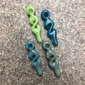 Puede incluir: Cuatro pipas de vidrio con un diseño de espiral retorcida. Una pipa es verde claro, una es azul verdoso sólido, una es azul verdoso oscuro texturizado y una es azul verdoso moteado. Cada pipa tiene un cuenco circular y un tallo largo y liso.