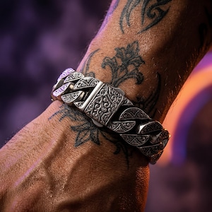May include: A silver-toned metal curb chain bracelet featuring intricate, engraved scrollwork patterns on each individual link and a central rectangular clasp, also decorated with detailed, ornate floral-inspired filigree engravings.