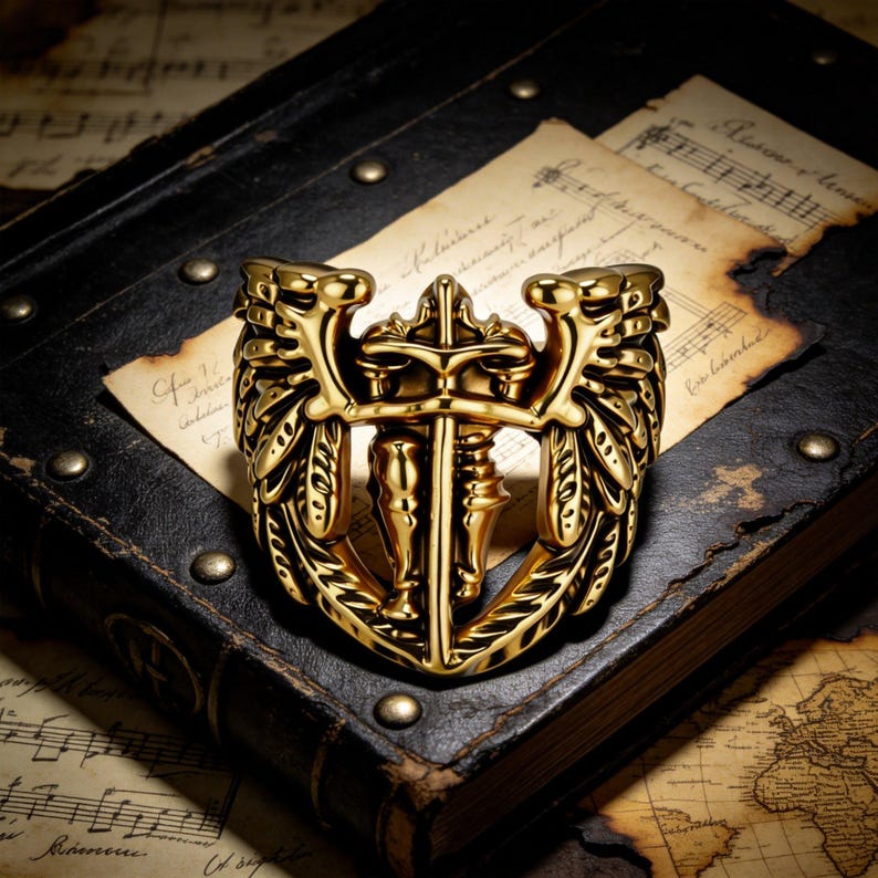 May include: A gold-colored ring with a detailed design featuring a knight holding a sword, flanked by ornate wings. The ring is set against a backdrop of aged sheet music and a leather-bound book, creating a vintage aesthetic.