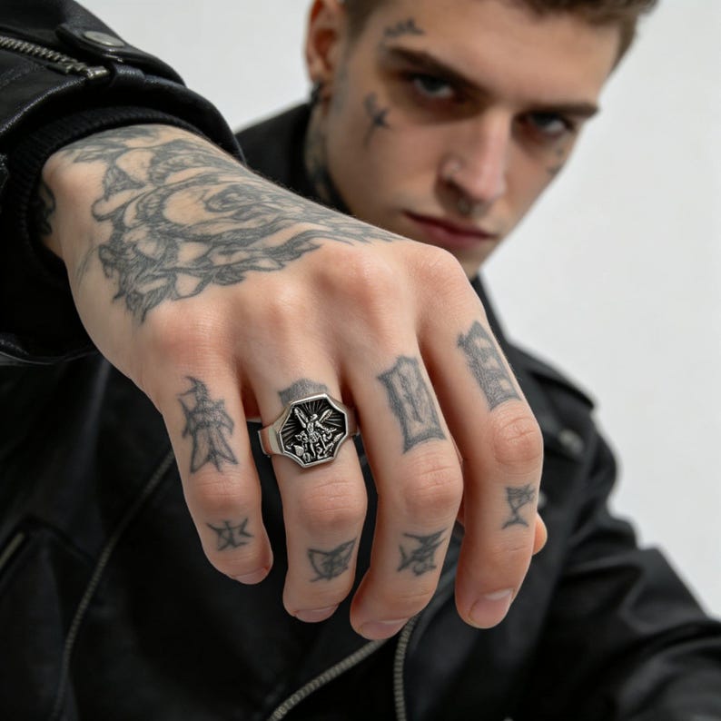 Peut inclure: Une bague argent&eacute;e avec une face octogonale orn&eacute;e d'un symbole religieux d&eacute;taill&eacute;. La bague est port&eacute;e au doigt, mettant en valeur son design complexe. La bague est un bijou.