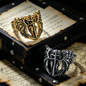 May include: Two rings with a shield and sword design. One ring is gold-colored, and the other is silver-colored. The rings are set against a backdrop of aged paper and a dark, textured surface, creating a vintage aesthetic.