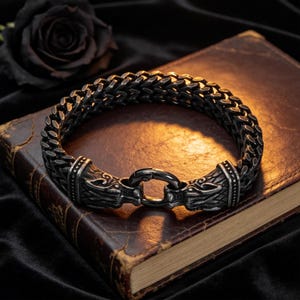 Puede incluir: Una pulsera de cadena de metal en tono plateado oscuro con un diseño de eslabones trenzados gruesos. La pulsera termina en dos motivos detallados de cabezas de animales que se unen en el centro mediante un cierre de resorte circular.