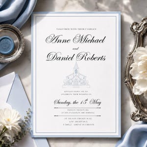 May include: A formal wedding invitation with a light blue border and text. The invitation includes the names Anne Michael and Daniel Roberts, a church illustration, and the date Sunday, the 15th of May. The invitation is surrounded by light blue fabric and decorative silver trays.