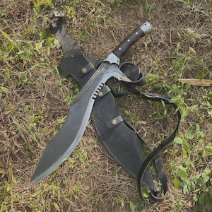 Puede incluir: Un cuchillo kukri curvo con mango de madera oscura y virola metálica, que presenta una hoja de acero ancha y afilada con el lomo dentado. El cuchillo viene acompañado de una funda de cuero negro con botones a presión de color latón y correa.