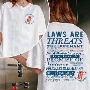 May include: White t-shirt with a cartoon bacon graphic and the text "YOU GUYS WANT TO MAKE SOME BACON?" on the front. The back of the shirt has the text "LAWS ARE THREATS" and other text.