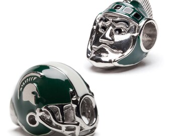 Puede incluir: Dos abalorios plateados con detalles verdes y blancos. Un abalorio es un casco de fútbol con el logotipo de Spartan. El otro abalorio es un casco espartano con una cara. Ambos abalorios tienen un agujero para una pulsera o collar.