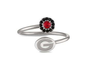 May include: A silver ring with a red stone surrounded by black stones and a white enamel 'G' on the band.