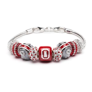 May include: A silver charm bracelet with red and white charms, including a charm with the letter "O" in white on a red background.