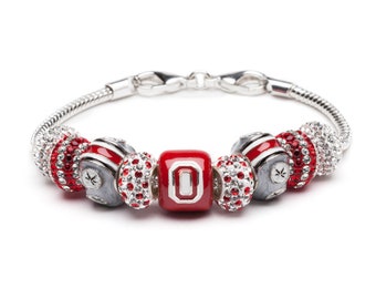 May include: A silver charm bracelet with red and white charms, including a charm with the letter "O" in white on a red background.