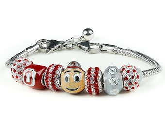 May include: A silver charm bracelet with red, white, and gray charms. One charm features the Ohio State Buckeyes mascot, Brutus Buckeye. Another charm features the letter "O" in red with a white outline. The bracelet has a silver clasp.