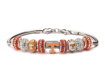 May include: A silver charm bracelet with orange and white beads featuring the University of Tennessee logo and the word "Tennessee".