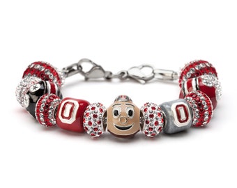 May include: A charm bracelet with red, white, and gray beads. The beads feature a cartoon mascot with a red and white hat, a silver charm with the letter "O", and a red and white bead with the letter "O".